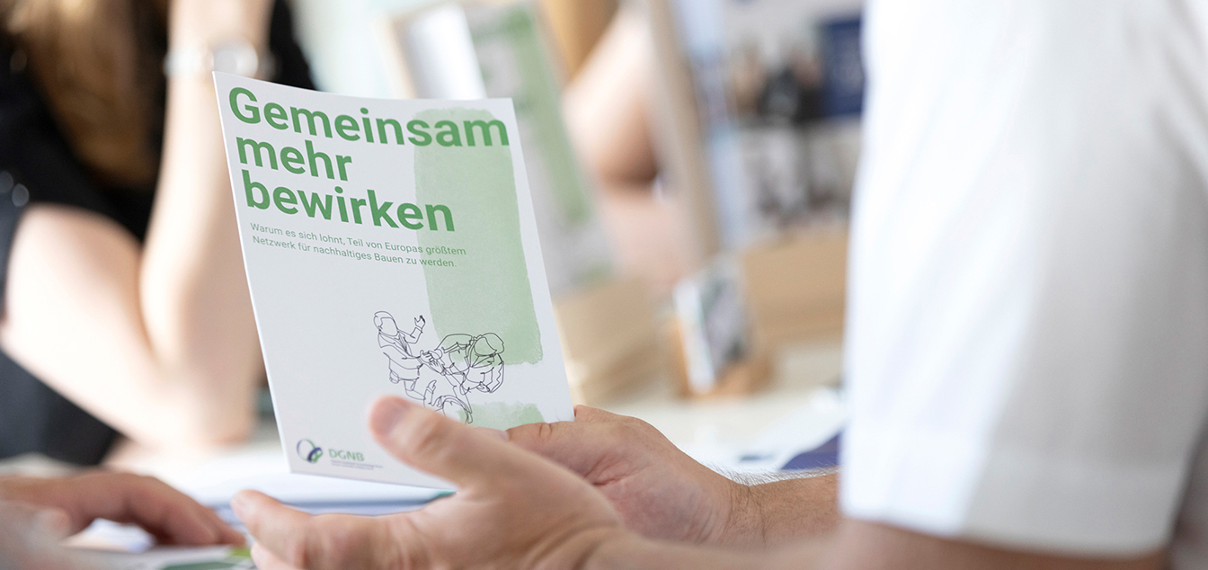 Eine sitzende person, von der nur der Oberarm zu sehen ist, hält die DGNB Mitgliederboschüre in den Händen.