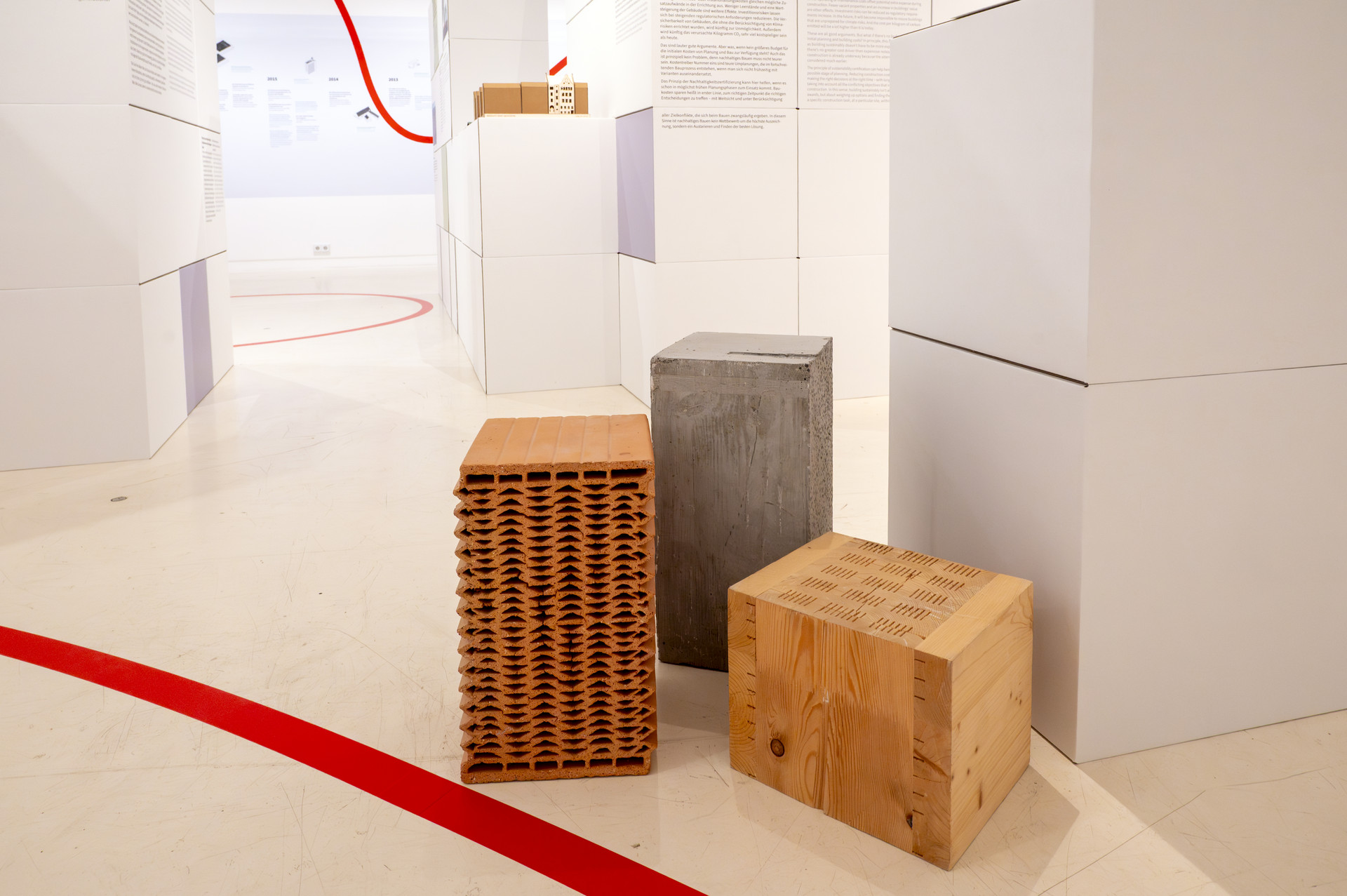 Im Fokus des Fotos sind 3 Kuben an Baumaterialen zu sehen. Ziegel, Beton und Holz