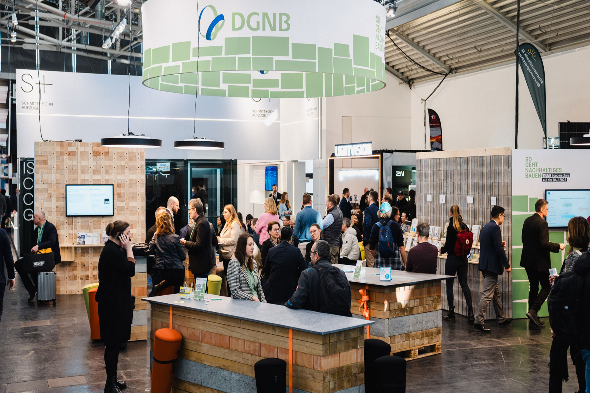 Das Foto zeigt einen Messestand der DGNB von der BAU 2025 mit Besuchenden. Auf dem Foto sind die verschiedenen eingesetzten modularen Elemente klar erkennbar