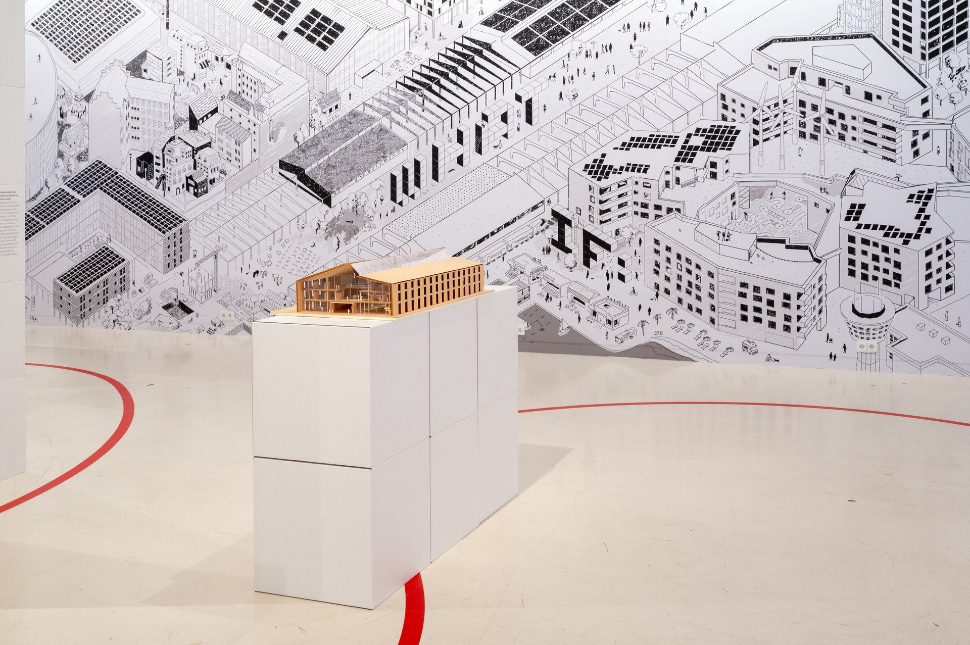 Einblick in die DGNB Ausstellung bei Aedes. Zu sehen ist im Hintergrund das Wandwimmelbild. Davor steht ein Gebäudemodell in braun. Auf dem Boden ist eine geschwungene rote Linie zu sehen.